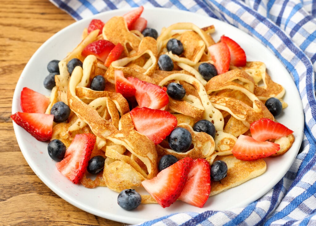 strings of pancakes on plate with berries
