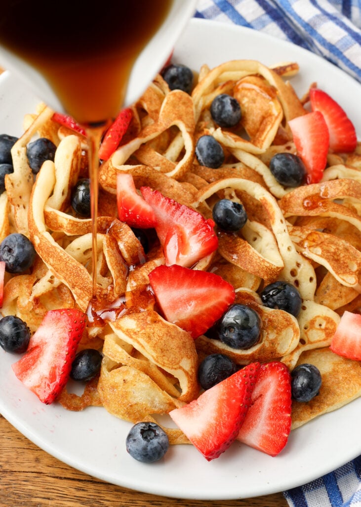pouring syrup over plate of pancakes with berries