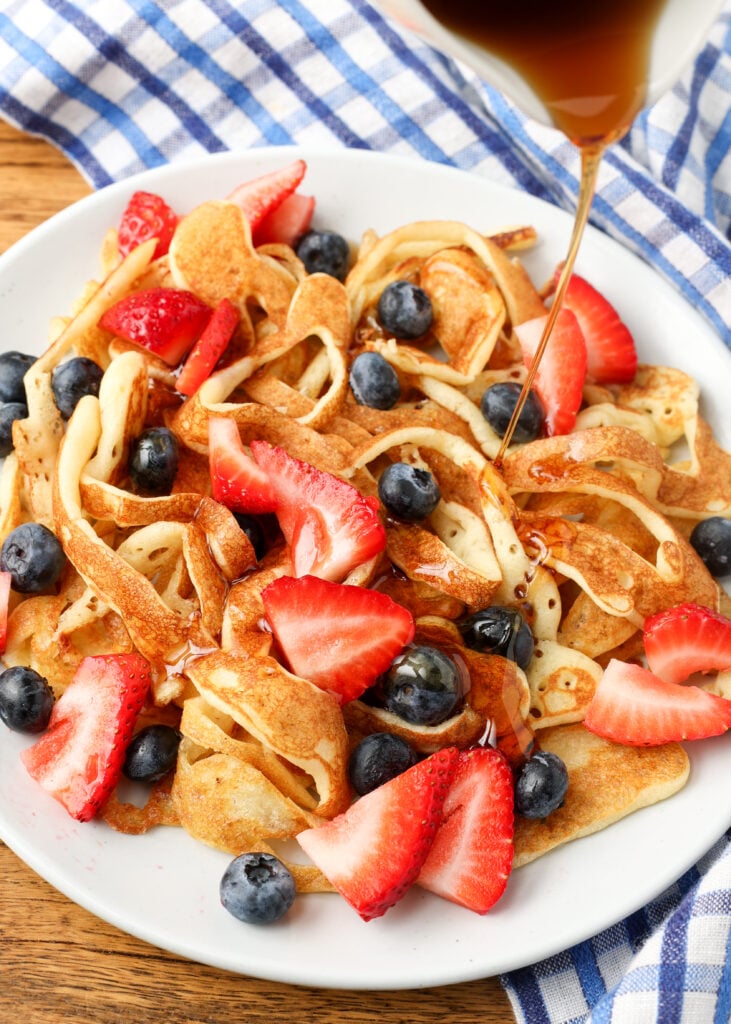 overhead shot of maple syrup being drizzled over pancakes with berries