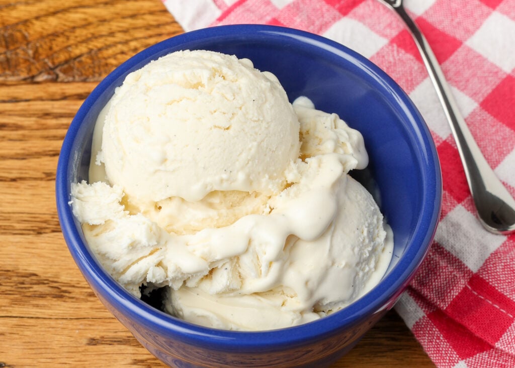 vanilla ice cream in a blue bowl next to a pink checked napkin 